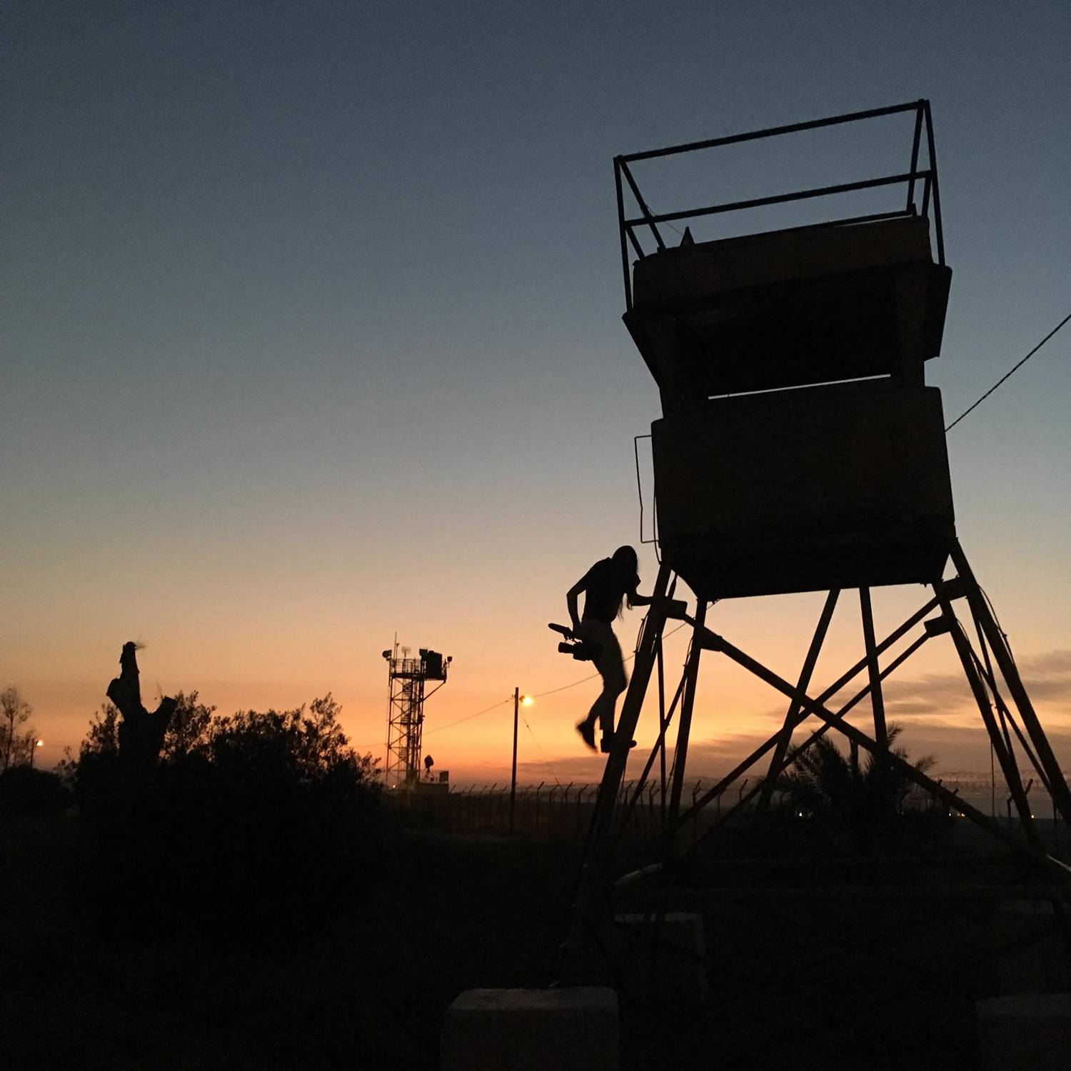 צללית של צלמת עולה על מגדל מים על רקע שקיעה