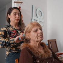 אישה מסרקת שיער לאמא שלה שיושבת על כיסא