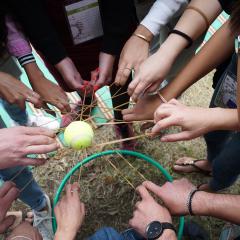 ידיים רבות במעגל אוחזות יחד חוטים וכדור טניס