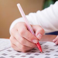 אילוסטרציה: יד אוחזת בעט ופותרת תשבץ