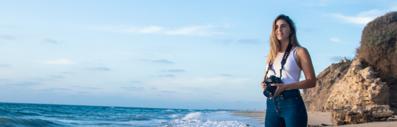 אישה צעירה עם מצלמה עומדת על חוף הים