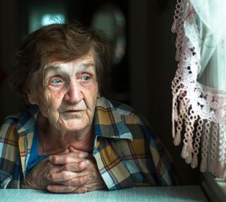 אישה זקנה בביתה מסתכלת מבעד לחלון