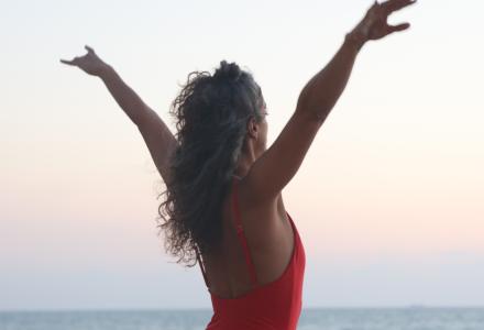 אישה עם ידיים פרוסות לצדדים מול הים