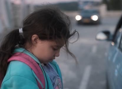 ילדה עומדת בכביש ליד רכב